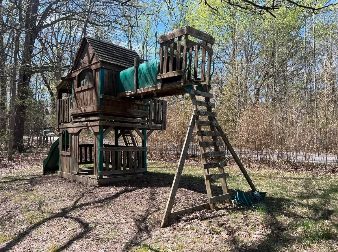 Weathered wooden backyard playset among leafless trees